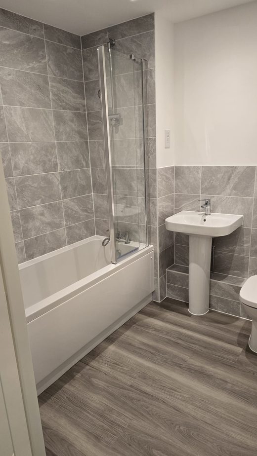 A tiled bathroom with clean bath, screen, basin and floor after a deep clean