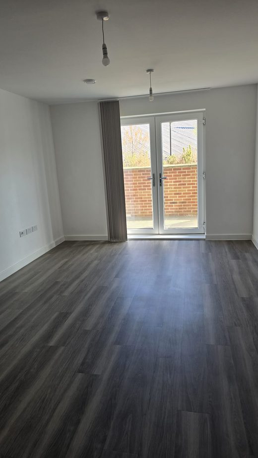 An empty living room with clean wood-effect flooring and patio doors