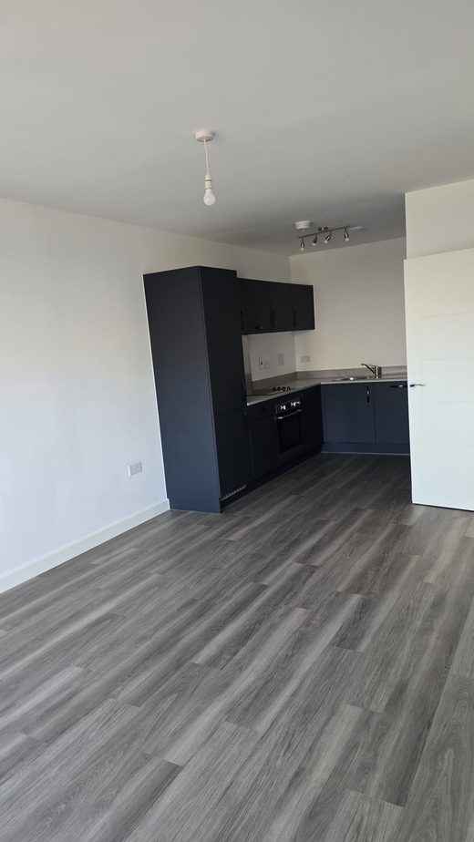 An empty open-plan living area and kitchen with clean floors, ready for handover